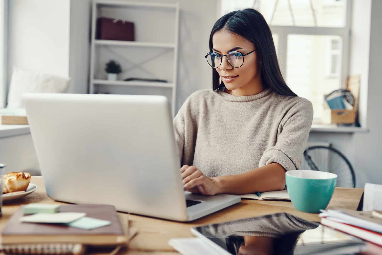 une femme aux longs cheveux noirs est assise et travaille derrière un ordinateur portable