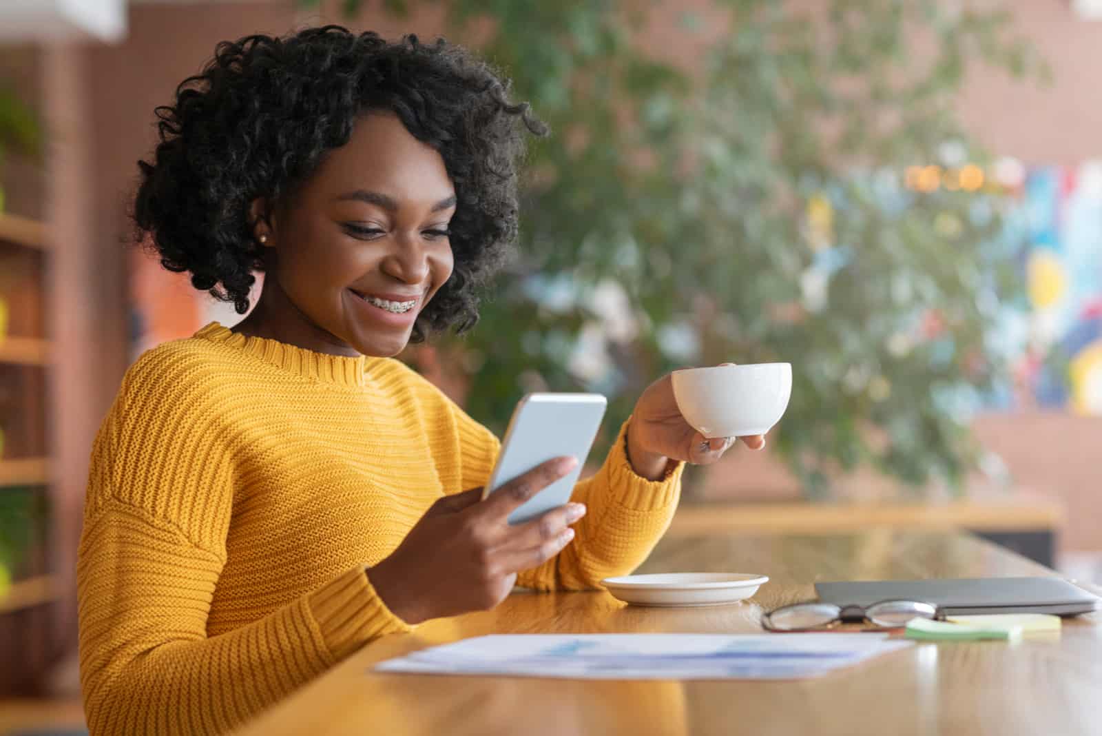 une femme souriante assise autour d'un café tenant un téléphone à la main