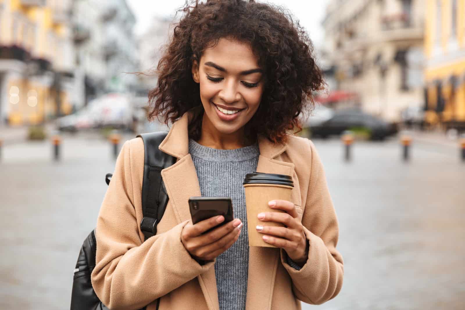 une femme souriante aux cheveux crépus se tient dans la rue et les boutons du téléphone