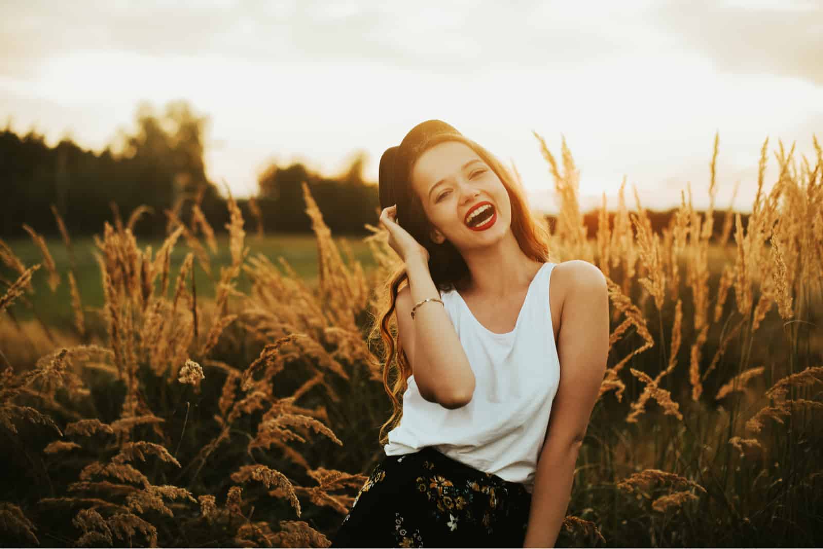 une femme souriante avec un chapeau sur la tête se dresse dans un champ