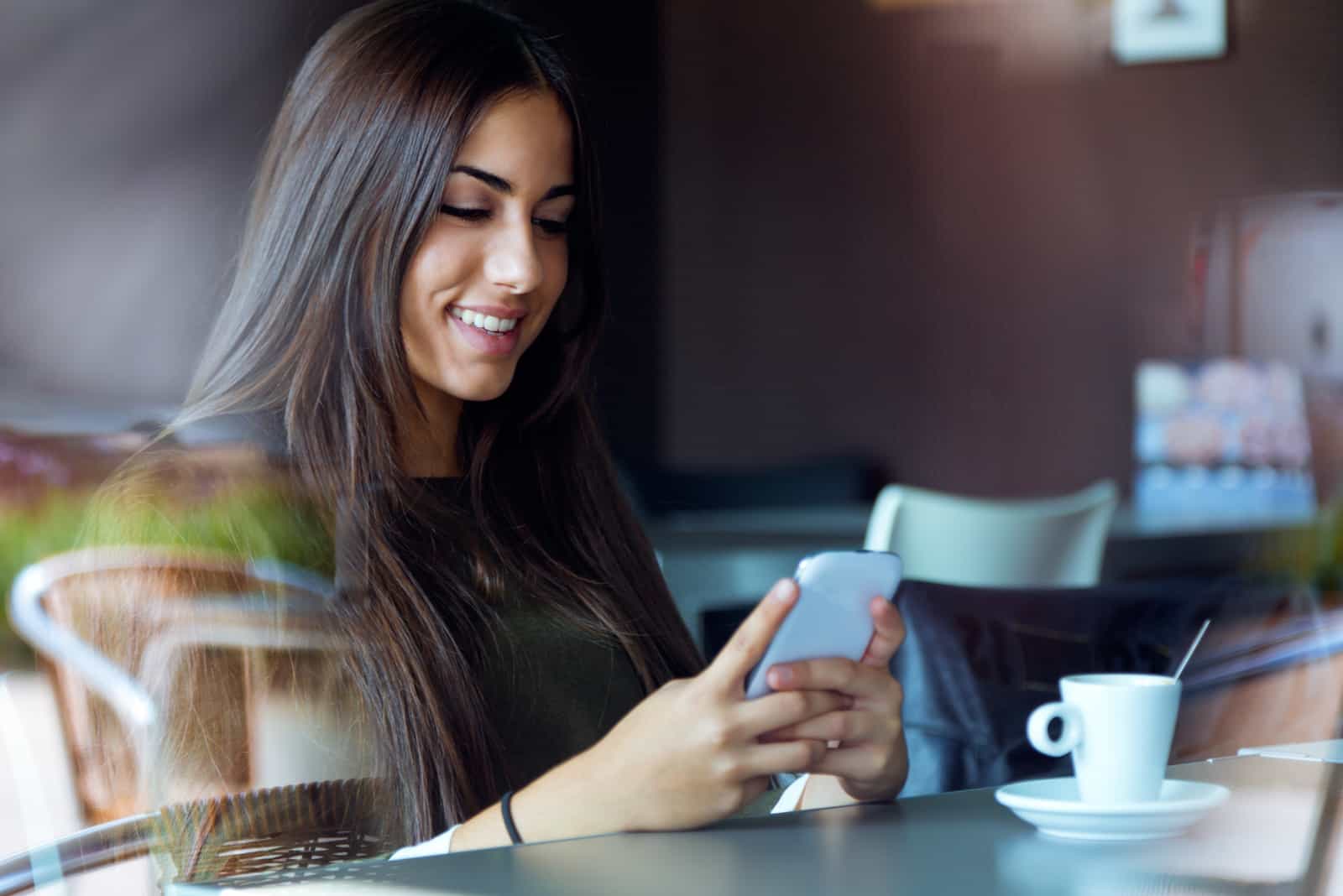 une belle femme aux longs cheveux noirs est assise à côté d'un bouton de café au téléphone