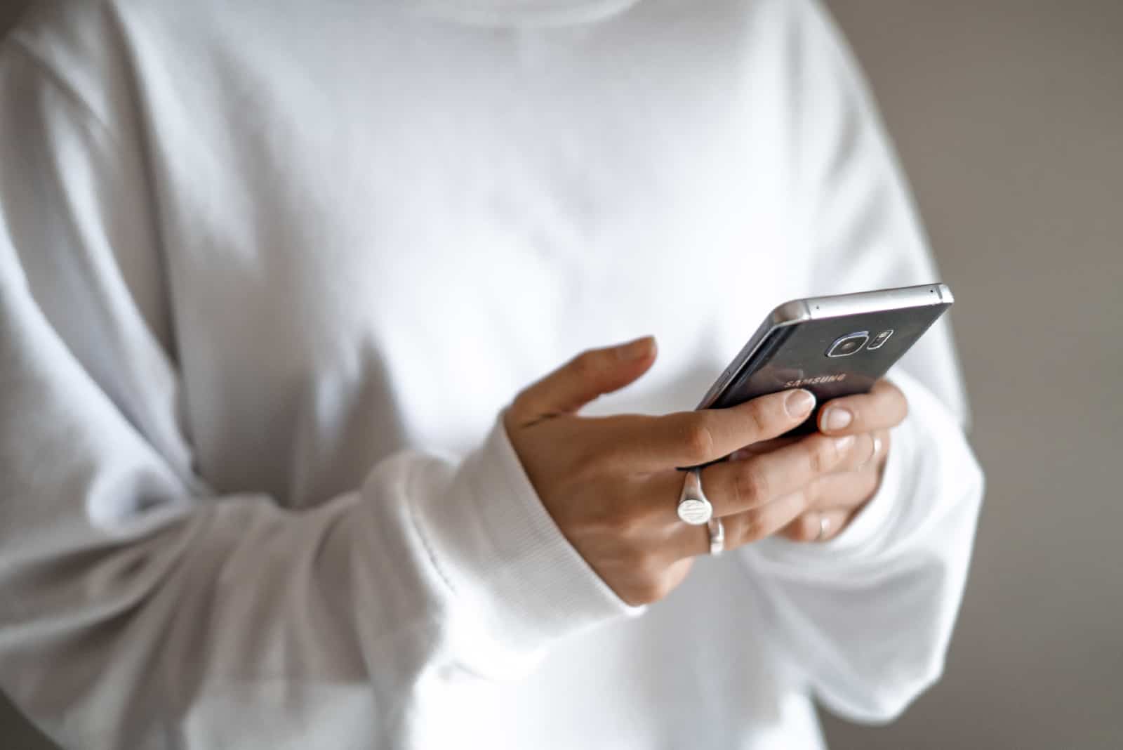 femme en sweat-shirt blanc tenant un smartphone