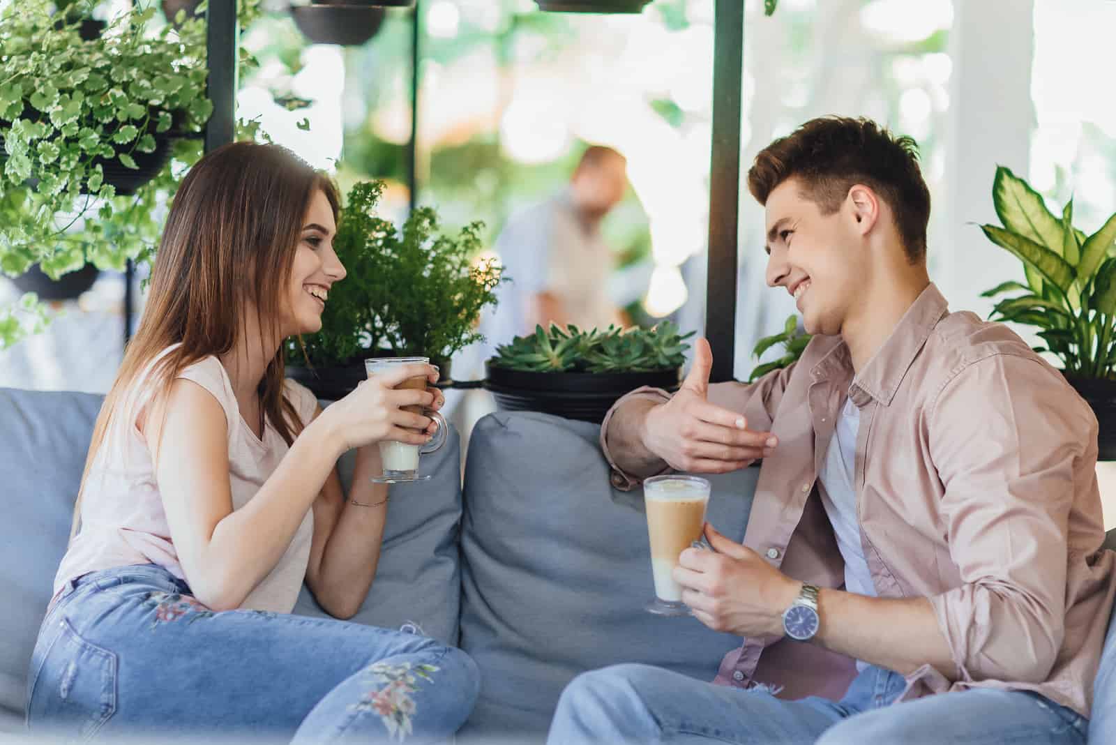 un homme et une femme assis sur le canapé boivent du café et parlent