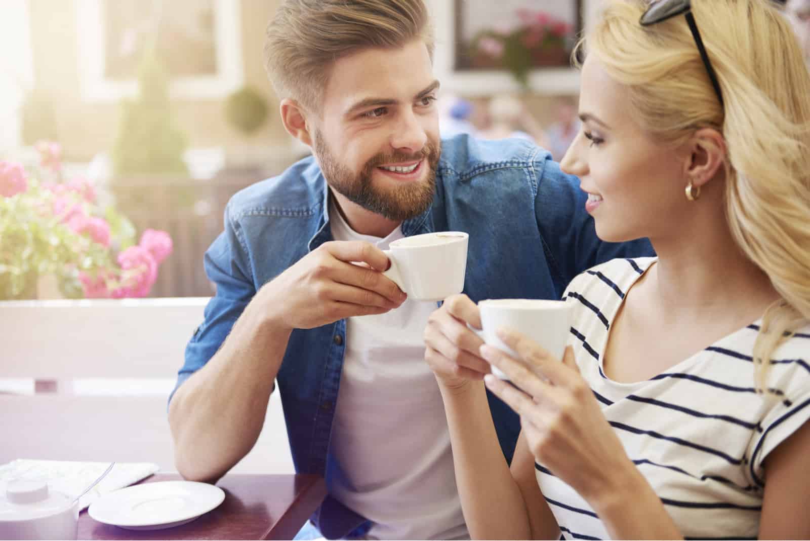 un homme et une femme aux cheveux blonds s'assoient à une table et boivent du café