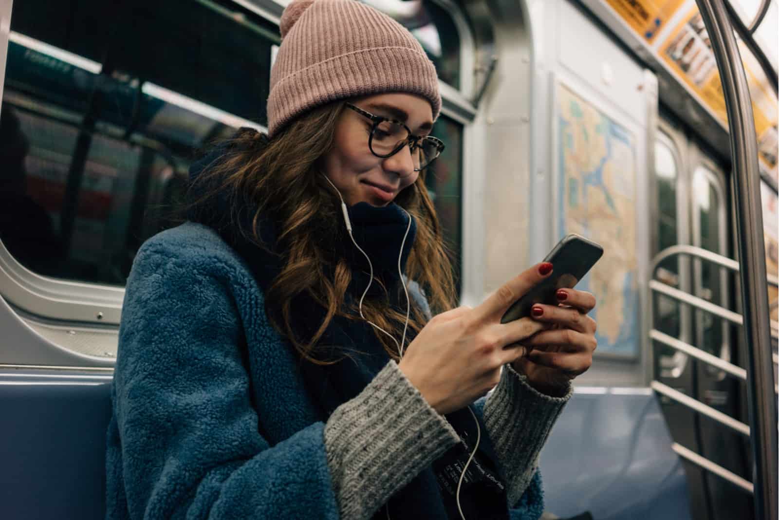 une belle femme aux longs cheveux bruns avec un chapeau sur la tête se tient dans le train et les boutons du téléphone