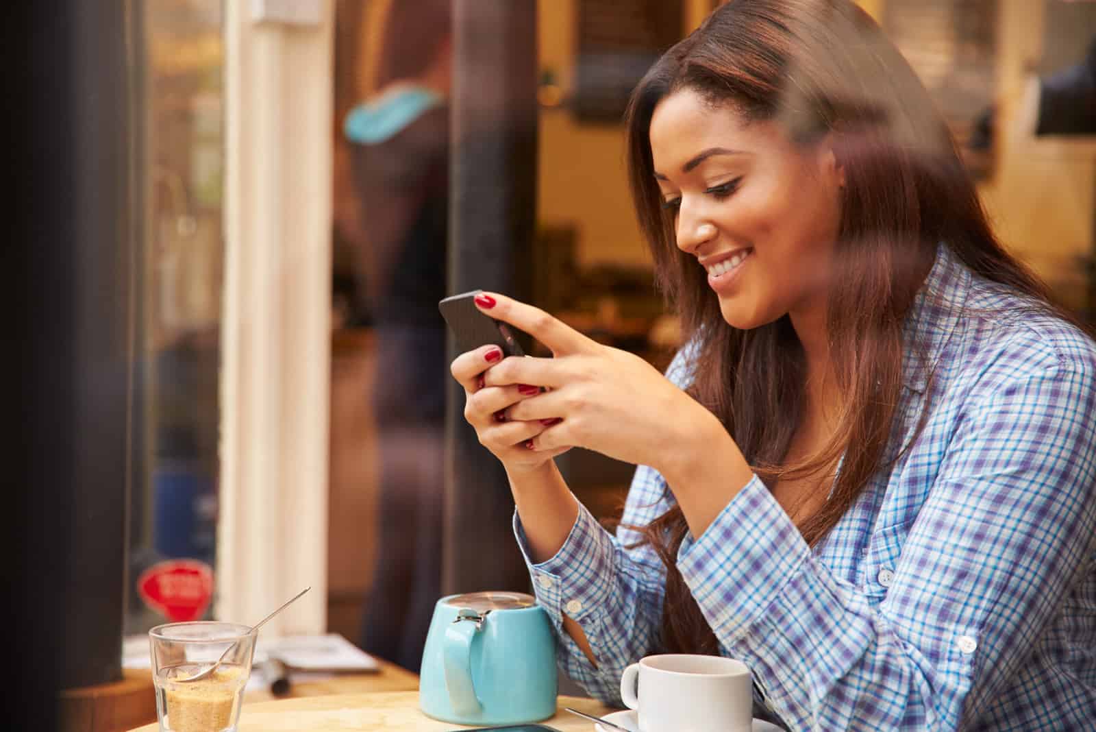une femme souriante assise dans un café et tapant au téléphone