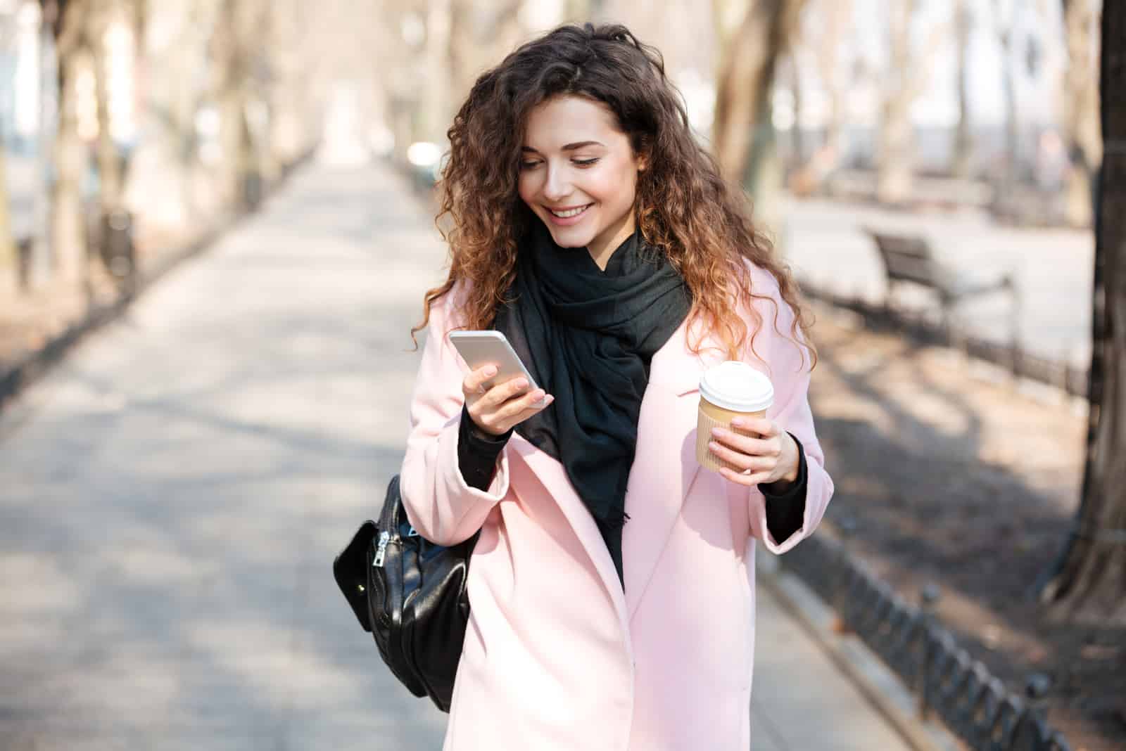 une femme souriante aux cheveux crépus se tient dans la rue tenant un téléphone à la main