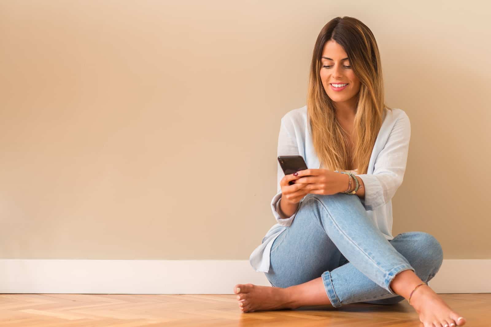 une femme souriante aux longs cheveux bruns est assise sur le sol et les boutons du téléphone