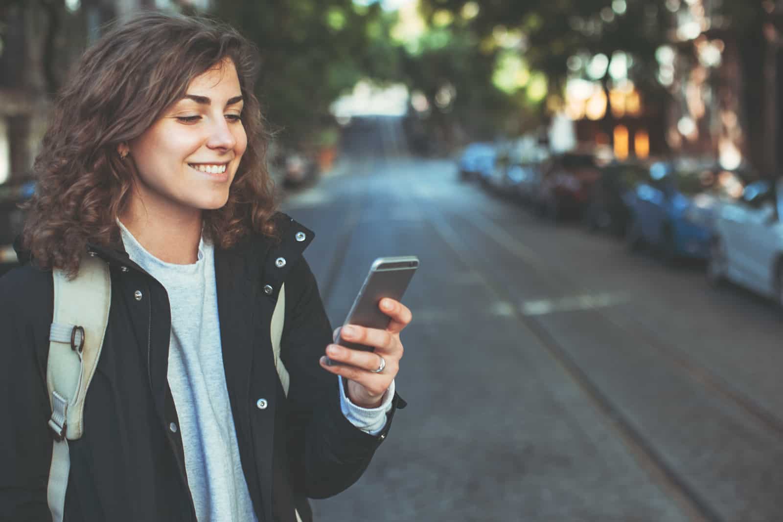 une femme souriante debout dans la rue et appuyant sur un téléphone