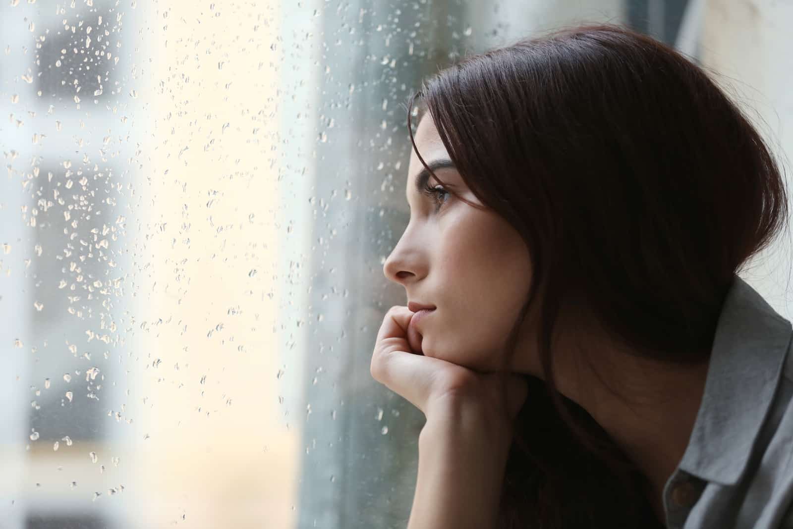 une femme triste est assise et regarde par la fenêtre