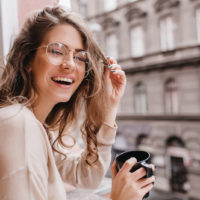 une femme souriante avec des lunettes boit du café