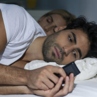 homme regardant son smartphone en étant allongé sur un lit