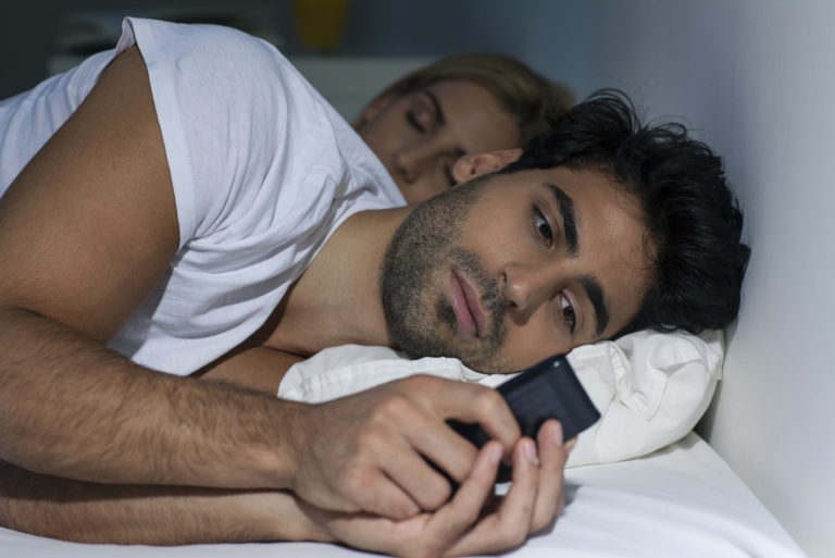 homme regardant son smartphone en étant allongé sur un lit