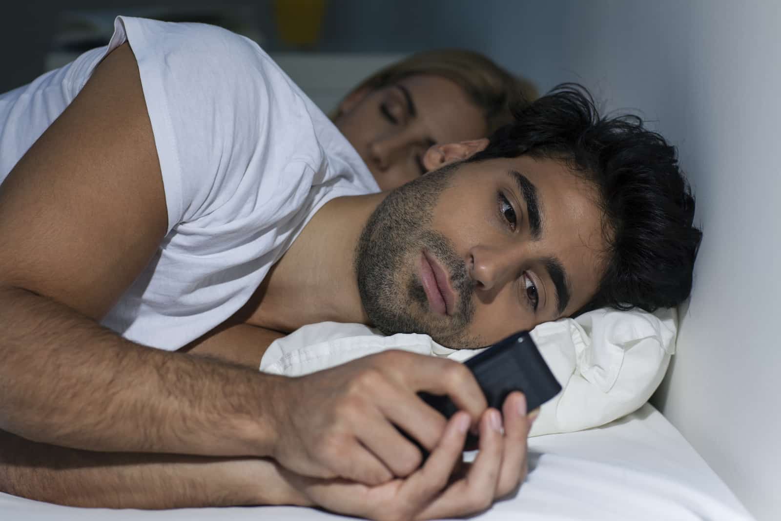 homme regardant son smartphone en étant allongé sur un lit