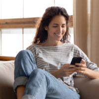une femme souriante est assise sur le canapé et les touches du téléphone