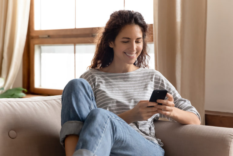 une femme souriante est assise sur le canapé et les touches du téléphone