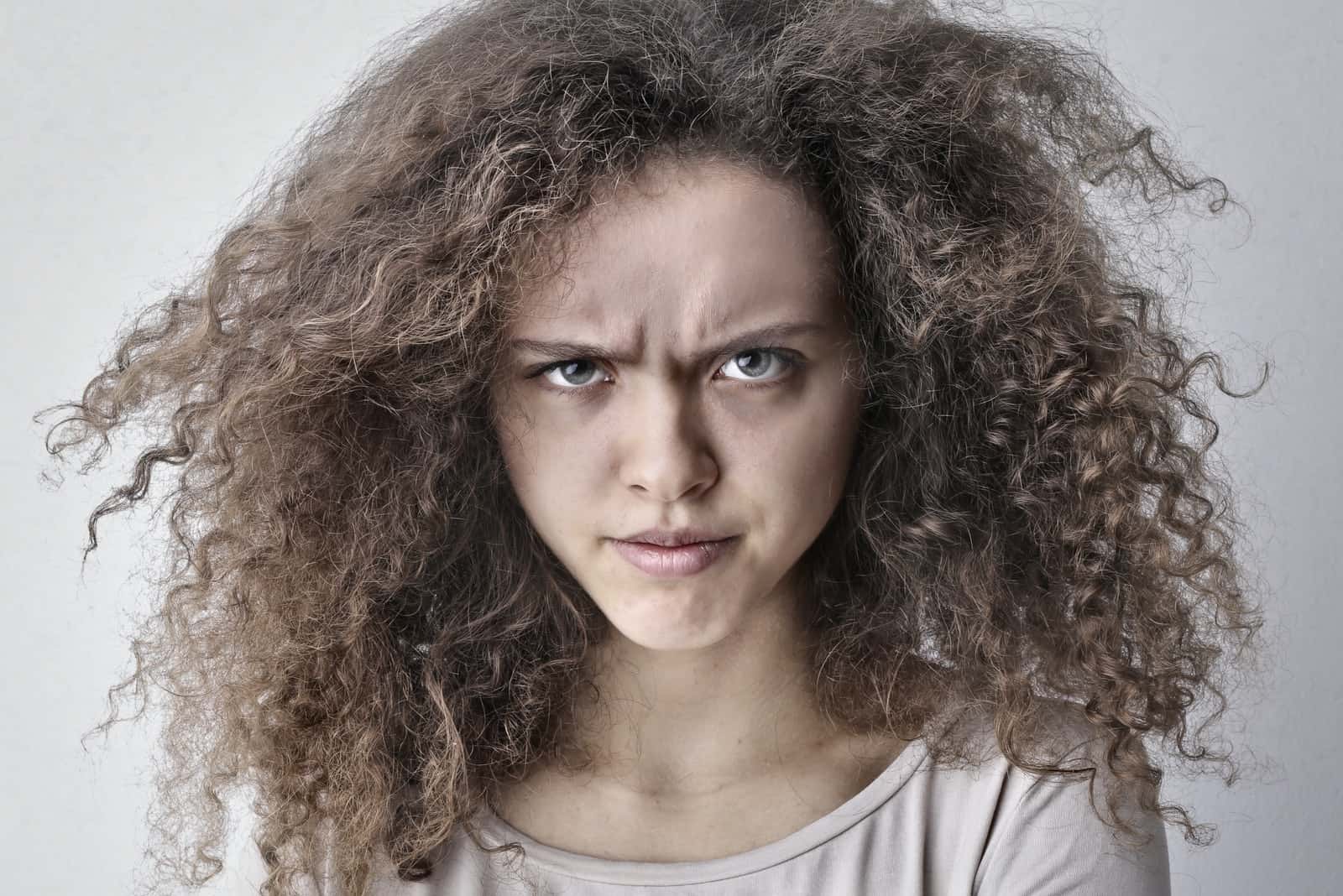 femme en colère avec des cheveux bouclés debout près d'un mur