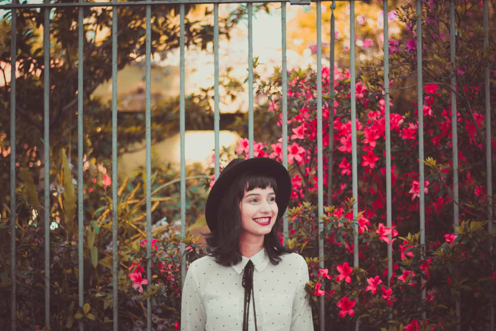 femme heureuse avec un chapeau debout près d'une clôture métallique