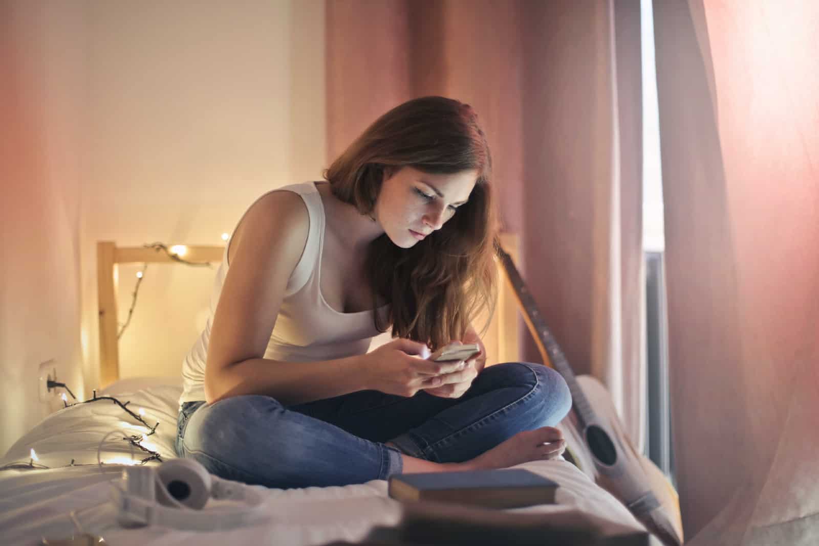 femme utilisant un smartphone en étant assise sur un lit