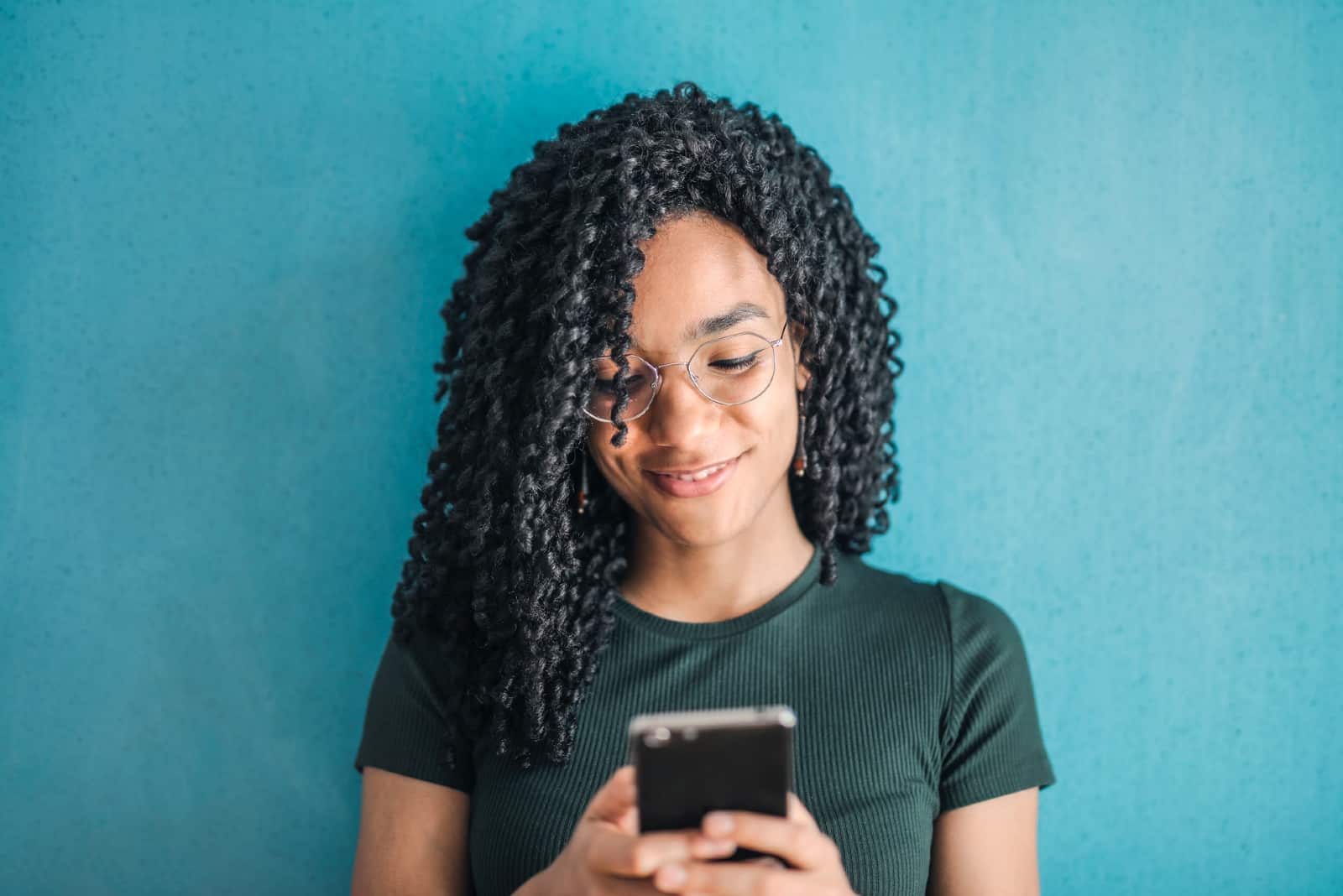 femme heureuse aux cheveux bouclés utilisant un smartphone