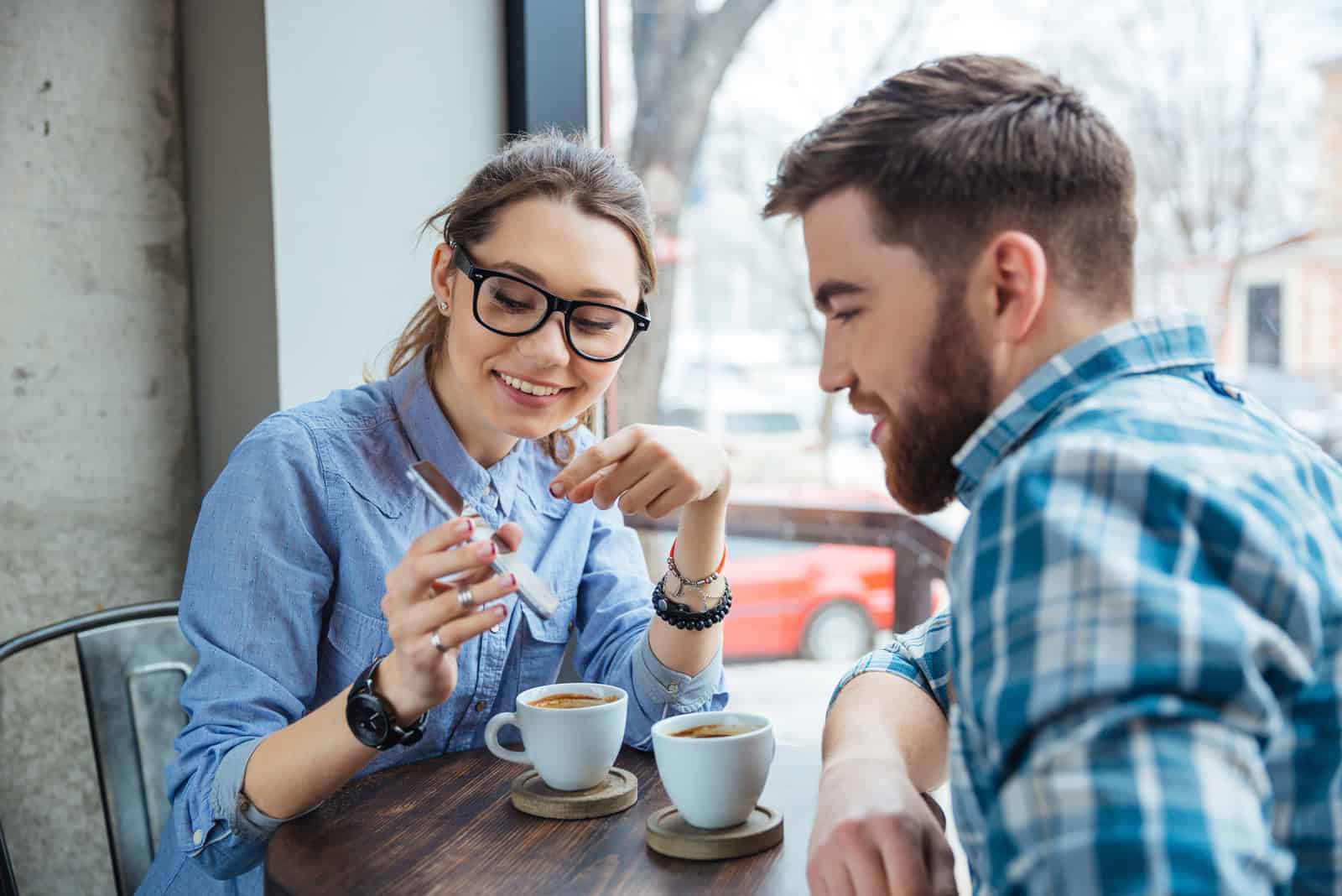 un homme et une femme sont assis dans un café et elle lui montre quelque chose au téléphone