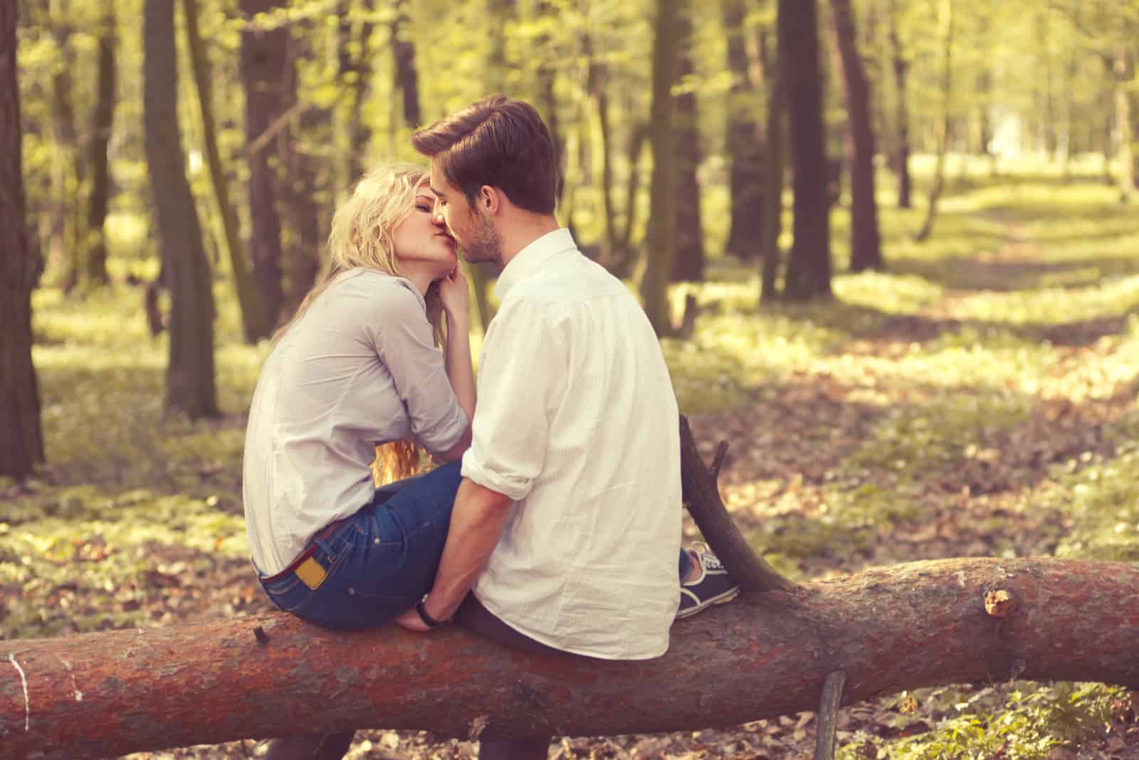 un homme et une femme sont assis sur un arbre et s'embrassent