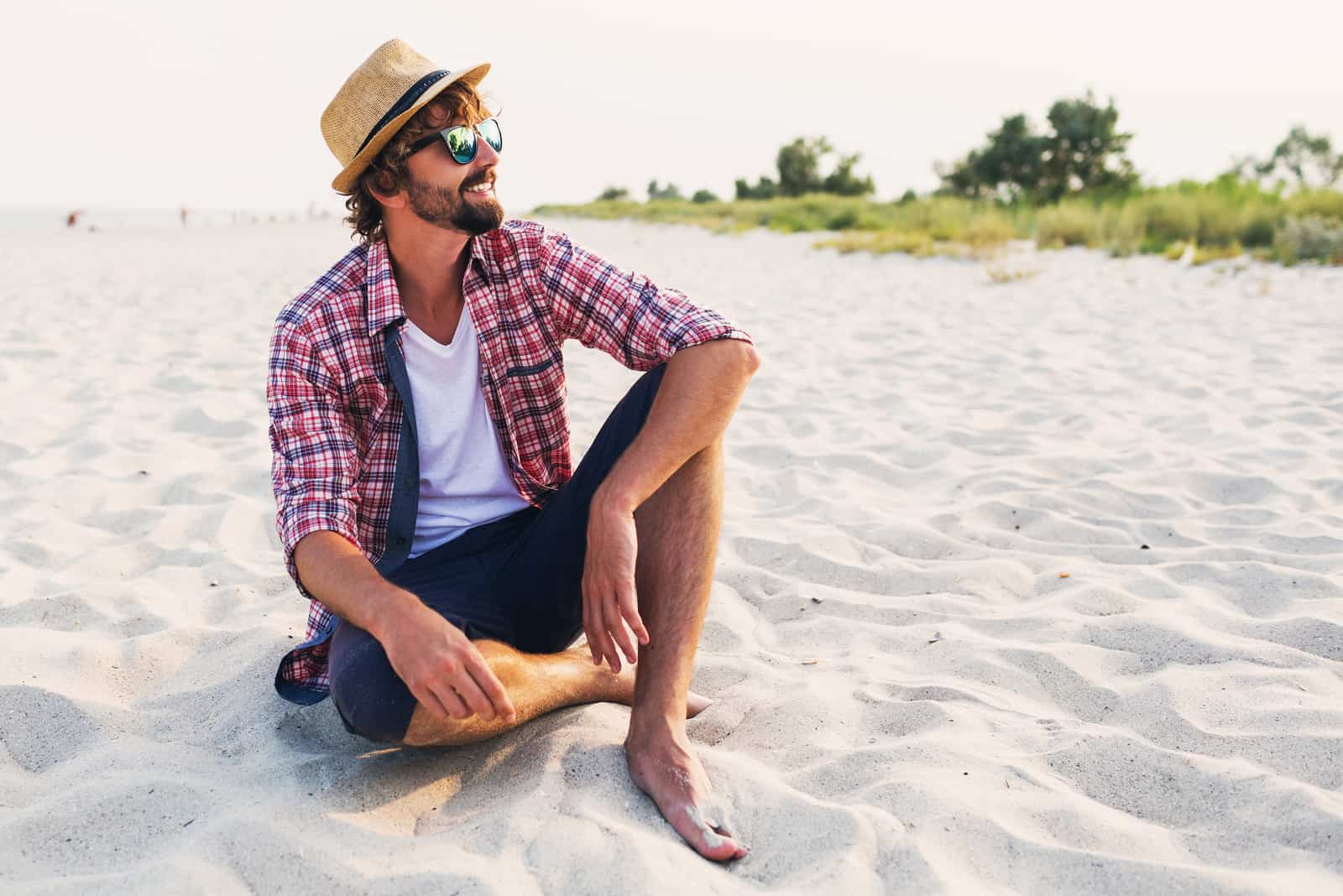 un homme souriant avec un chapeau sur la tête est assis sur la plage
