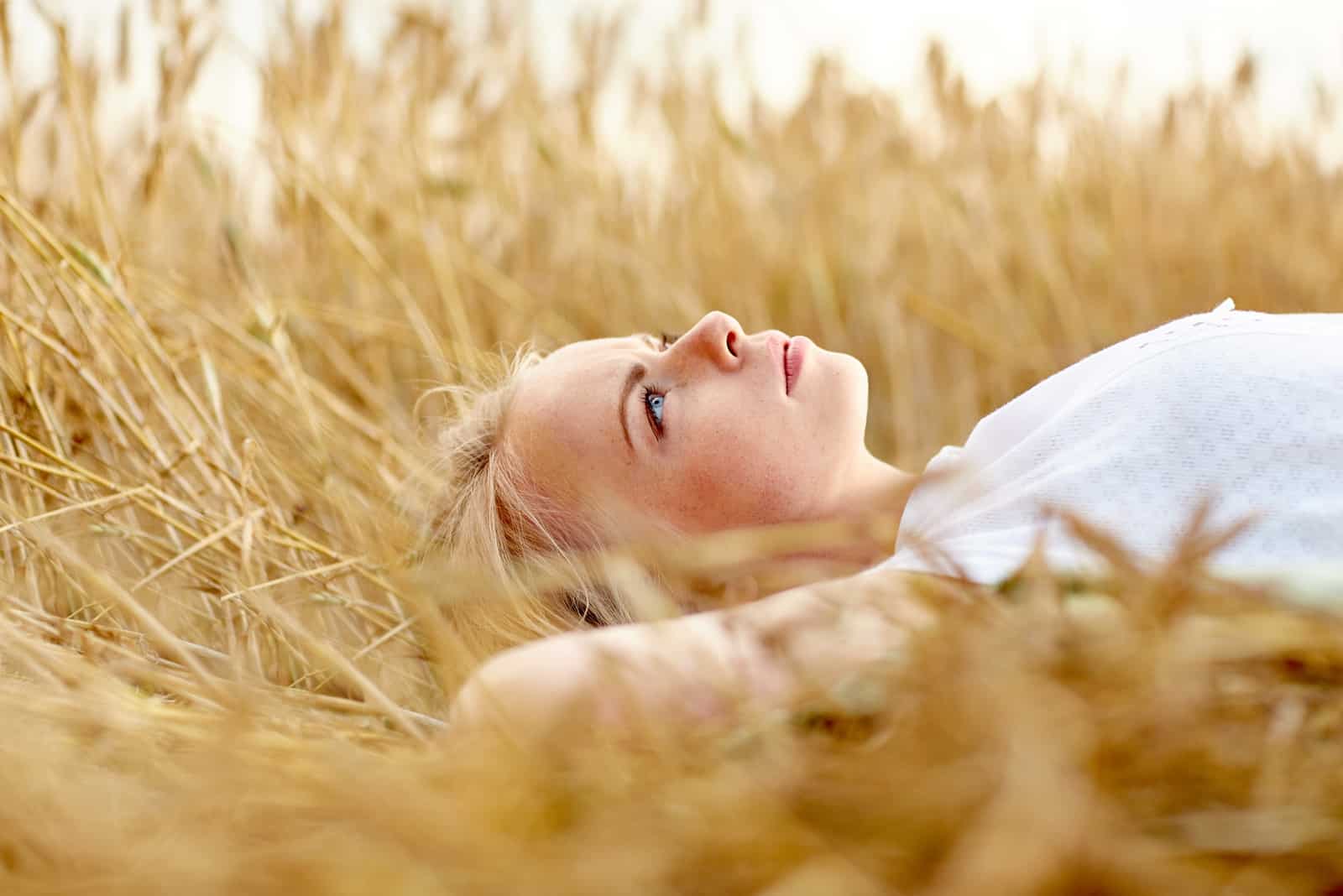 une femme aux cheveux blonds se trouve dans l'herbe et pense