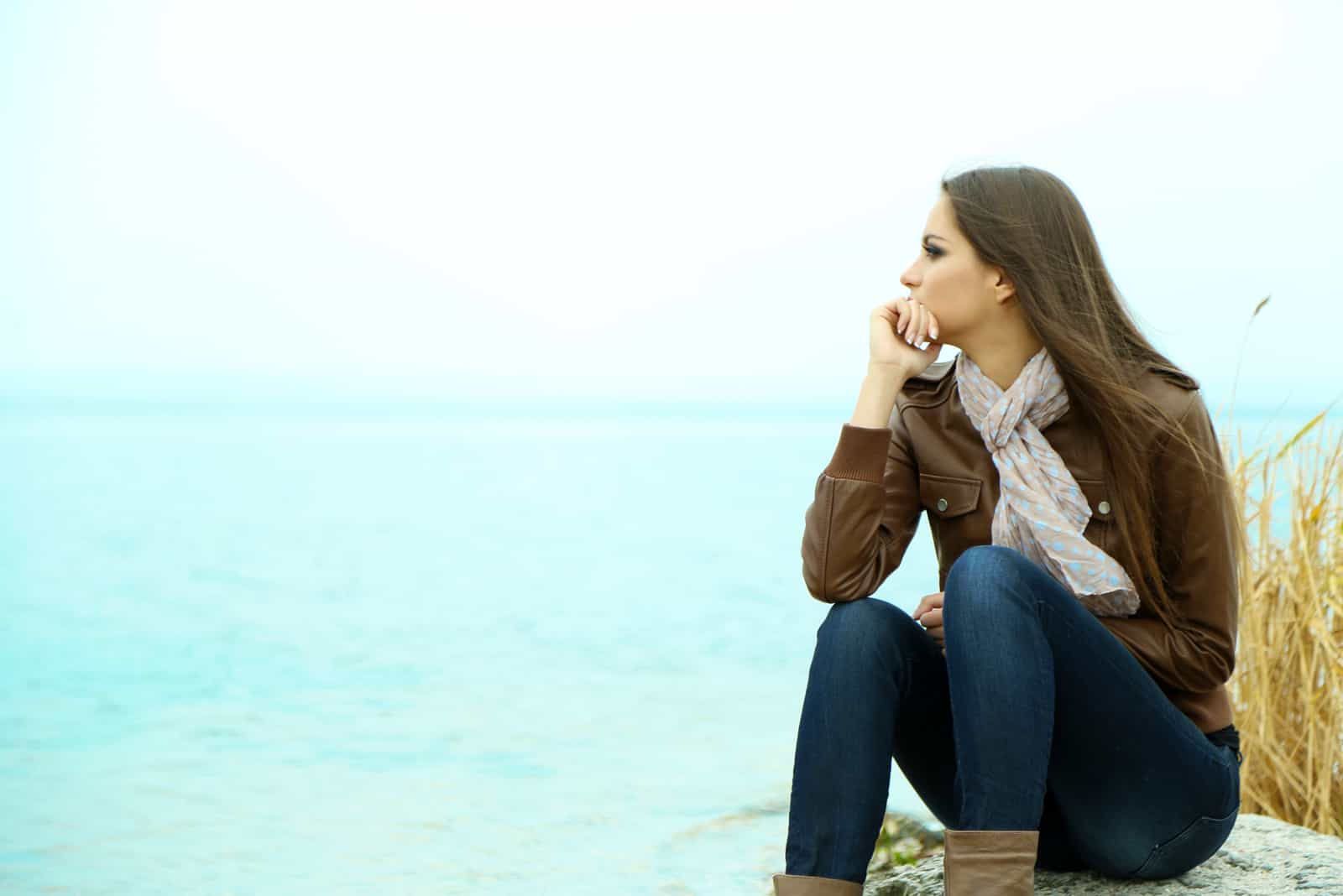 une femme imaginaire aux longs cheveux bruns est assise sur un rocher et regarde la mer