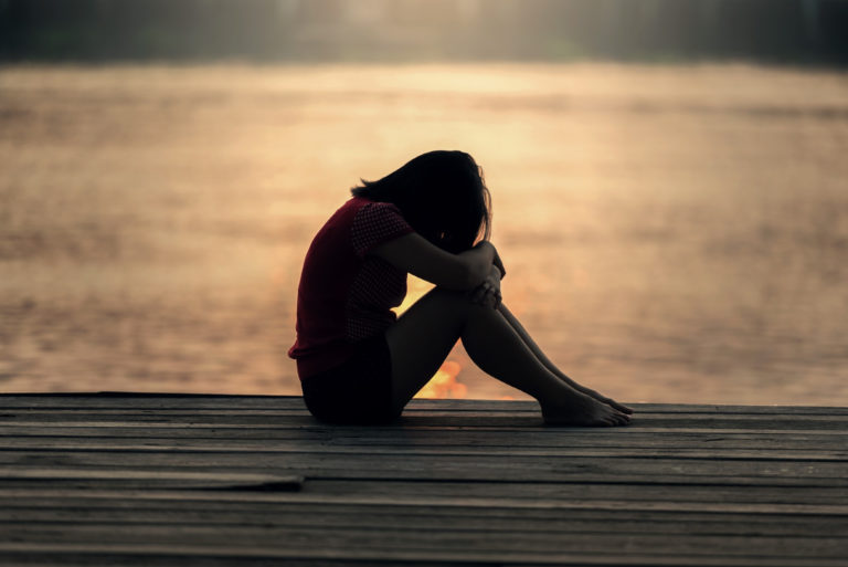 femme triste assise sur un quai près de la mer