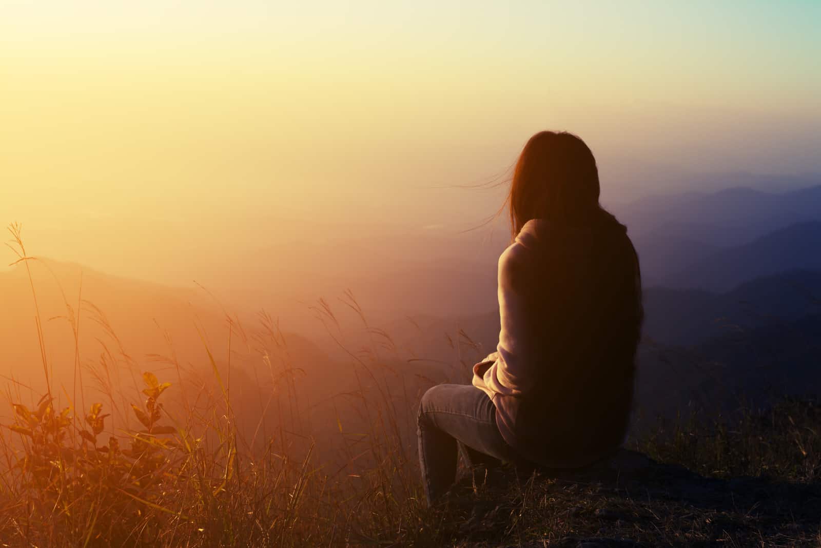 une femme triste est assise sur un rocher et regarde devant elle