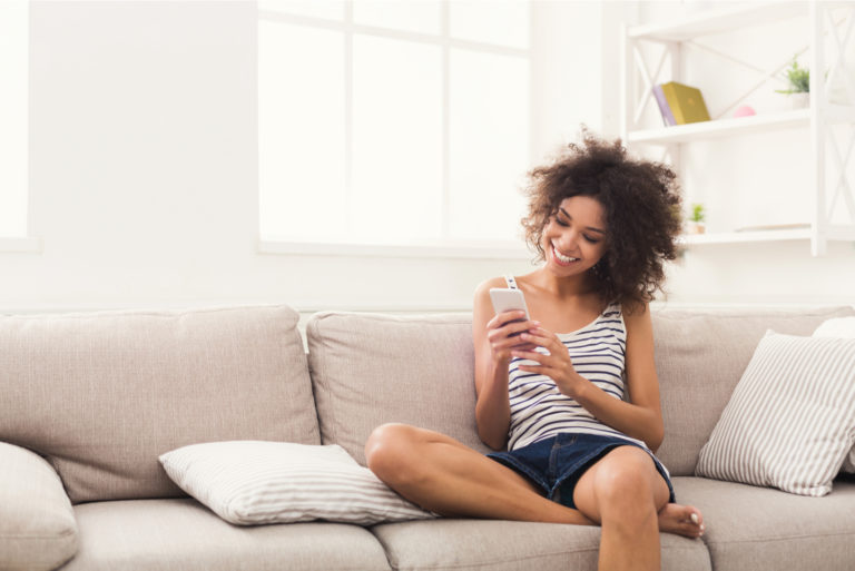 une femme souriante aux cheveux crépus est assise sur le canapé et les touches du téléphone