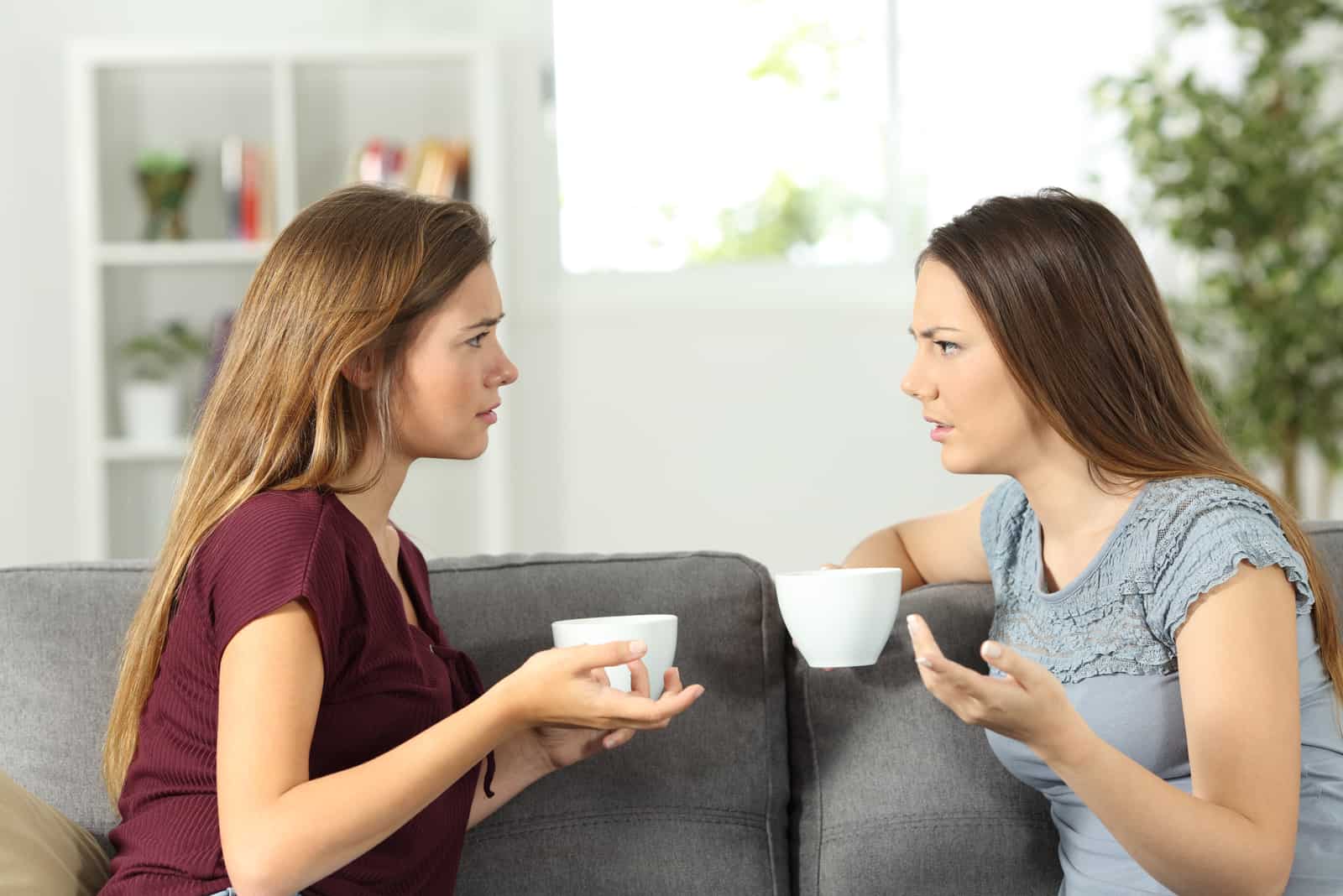 deux femmes buvant du café et parlant assises sur le canapé
