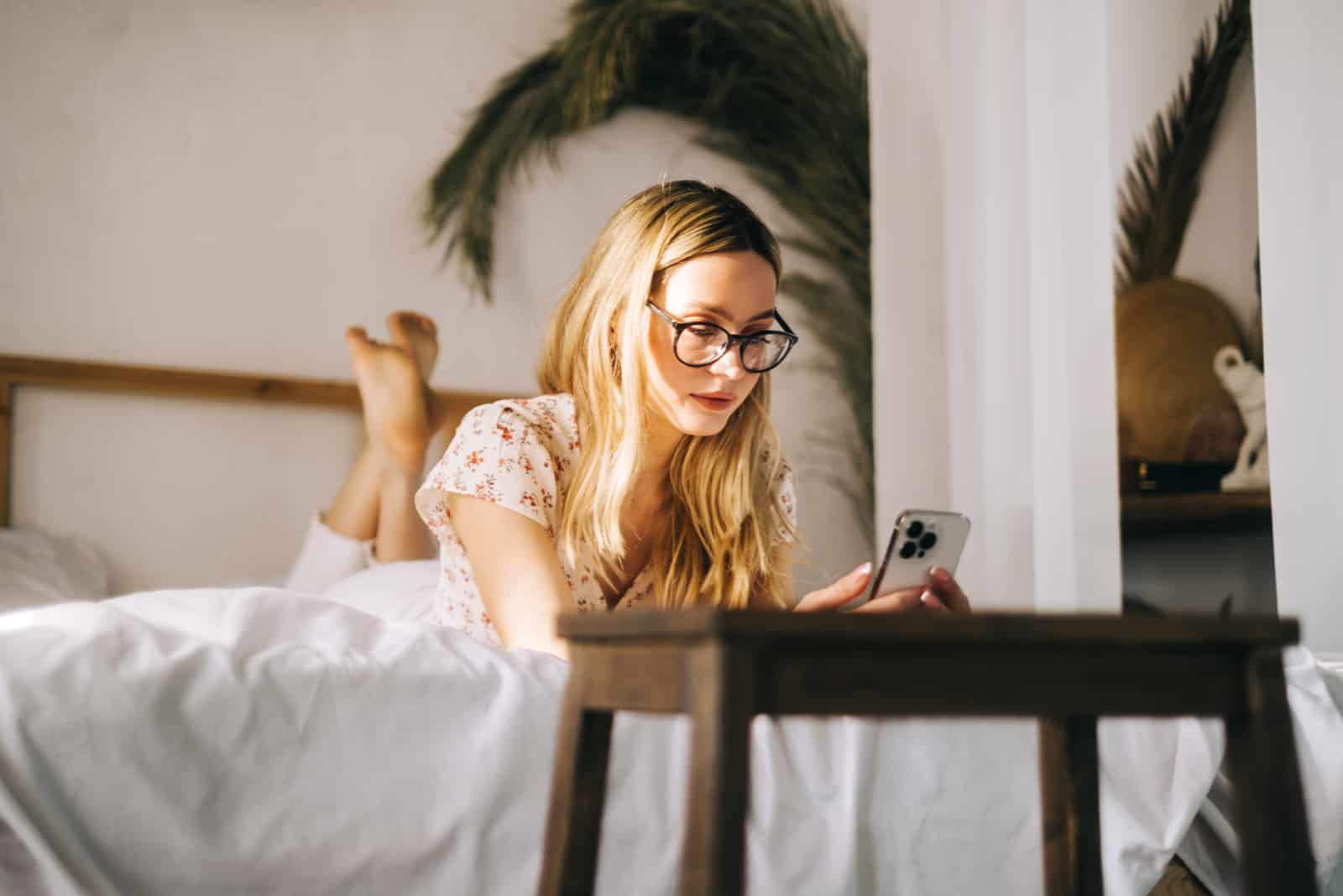 femme blonde se trouve dans son lit et tient le téléphone