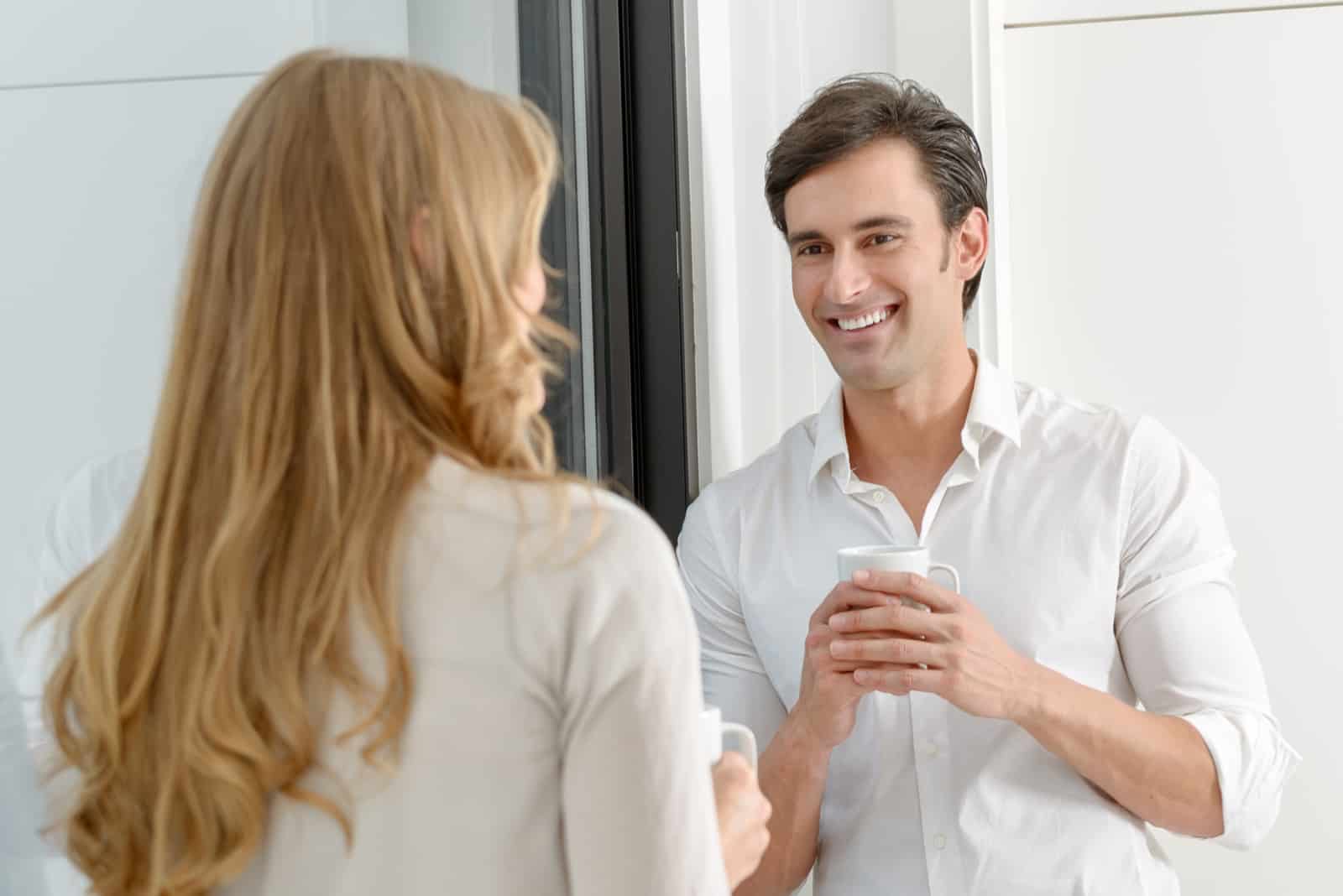 un homme debout dans l'embrasure de la porte tenant une tasse de café et parlant à une femme