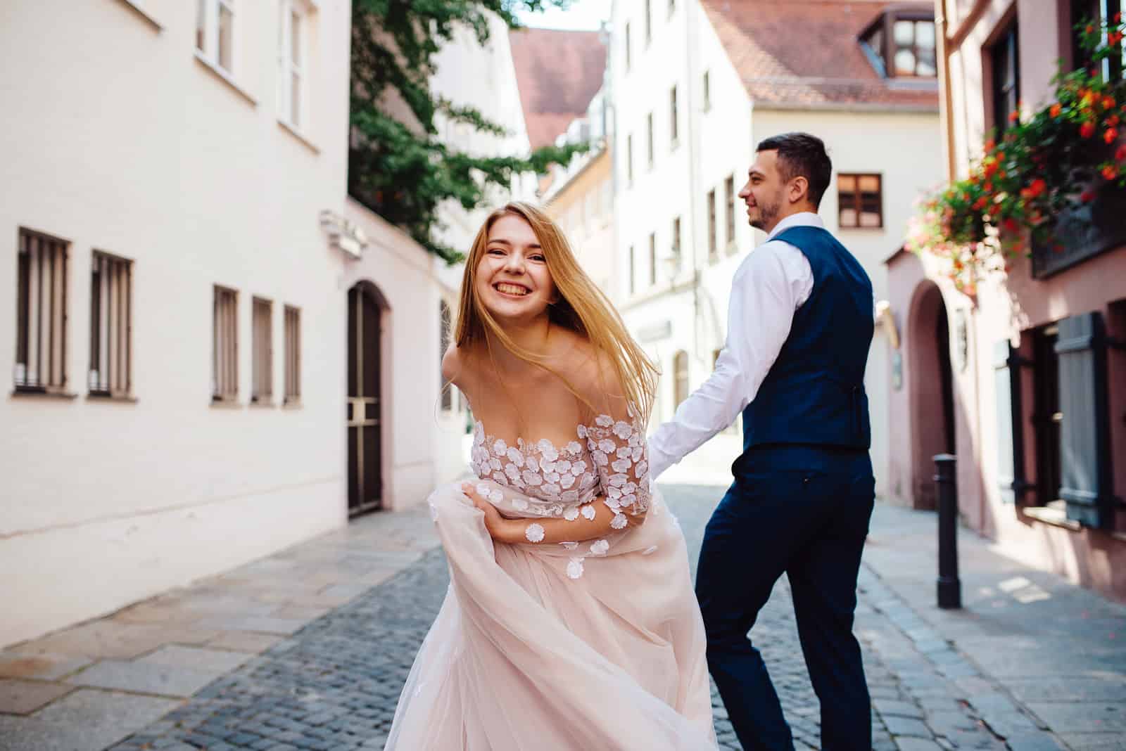 un homme et une femme marchent sur les pavés en robe de mariée