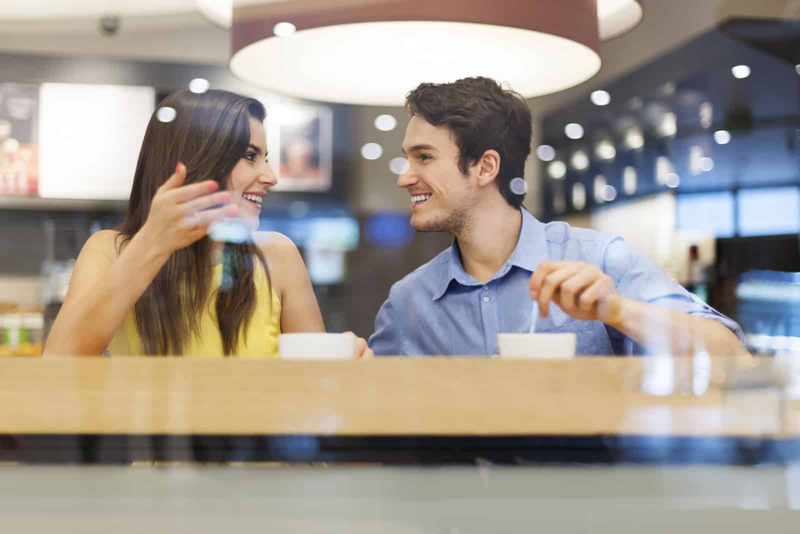 un homme et une femme sont assis dans un café et parlent autour d'un café