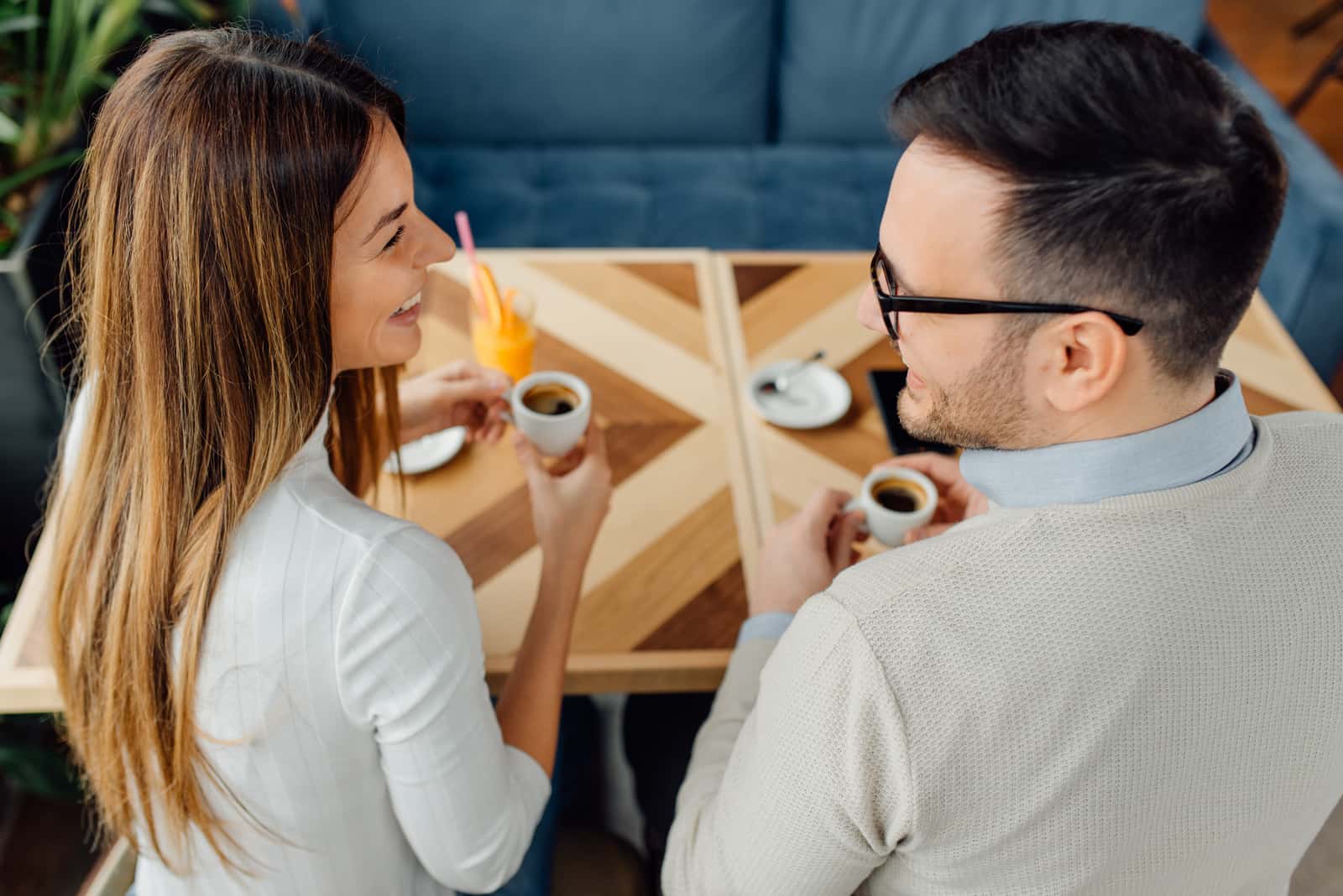 une femme aux longs cheveux bruns assise à une table avec un homme et parlant