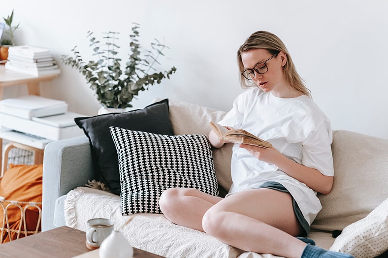 une femme lisant le livre assise sur le canapé à la maison
