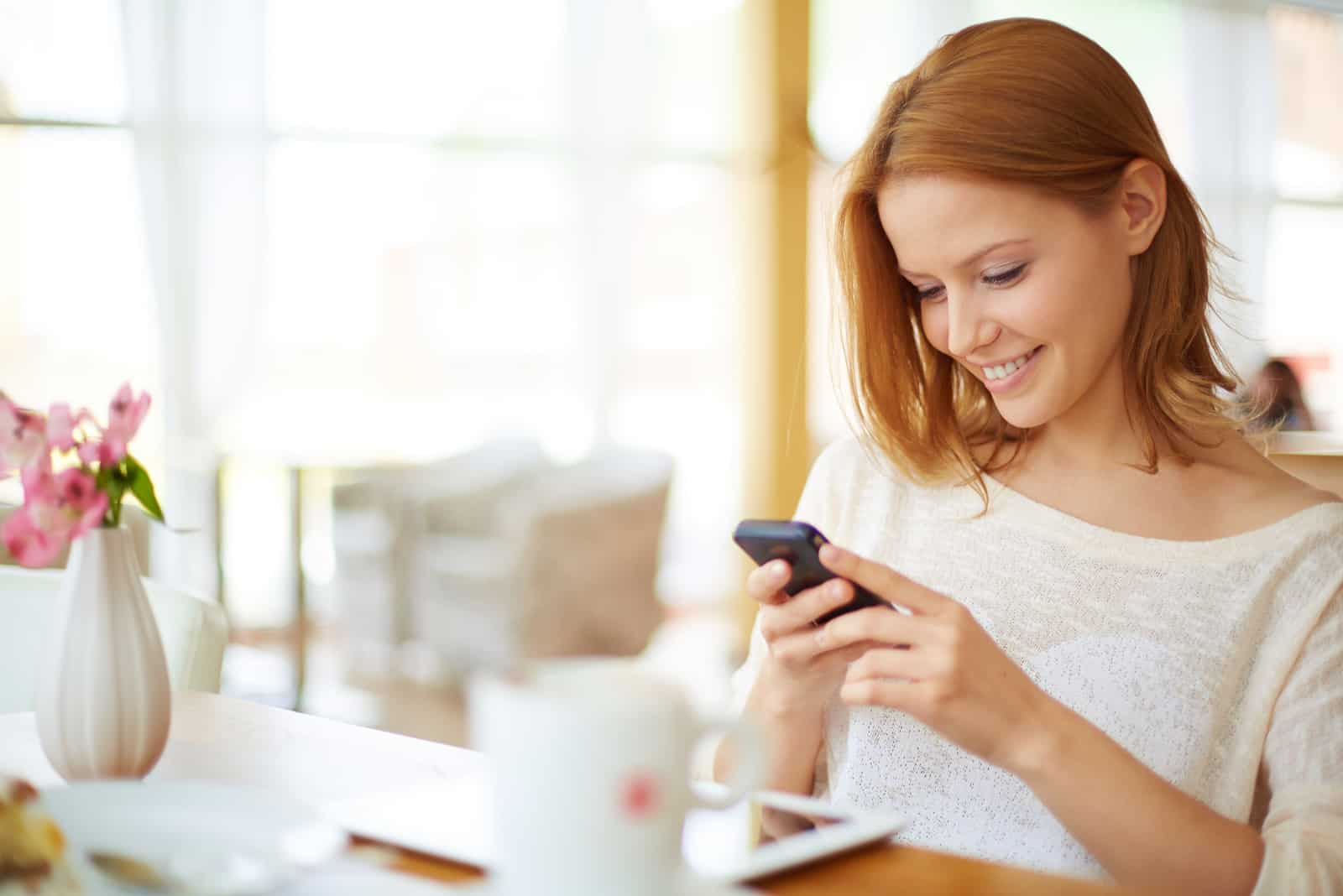 une femme rousse souriante est assise à une table et les touches du téléphone