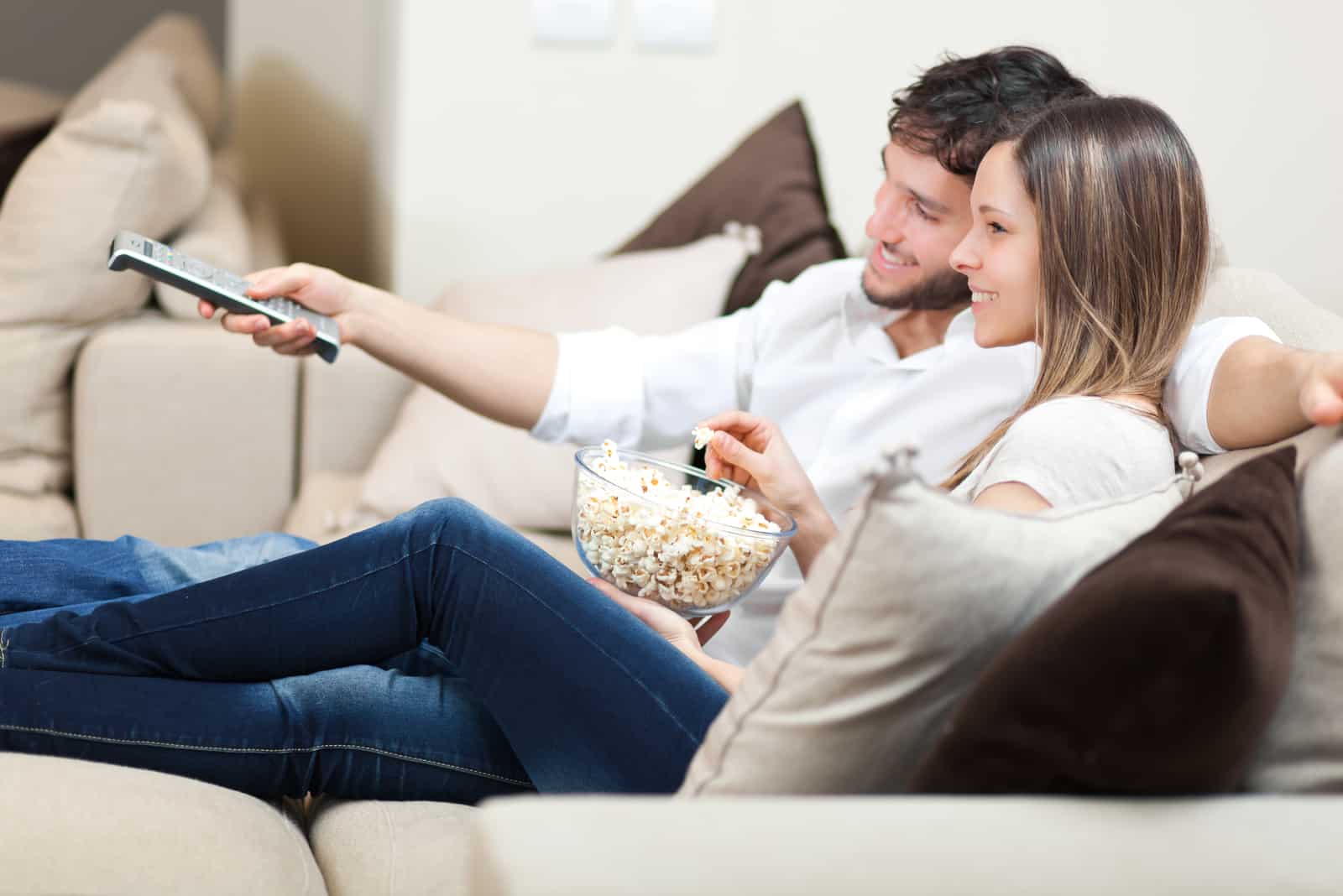 une femme souriante allongée à côté d'un homme mangeant du pop-corn et regardant la télévision