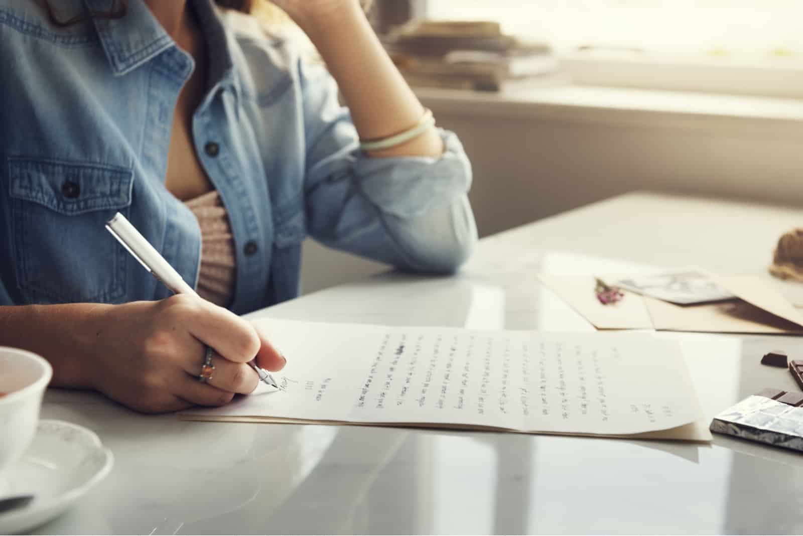une femme est assise à une table et écrit une lettre