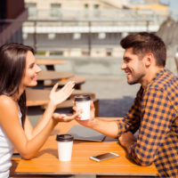 un homme et une femme sont assis à une table à l'extérieur et parlent autour d'un café