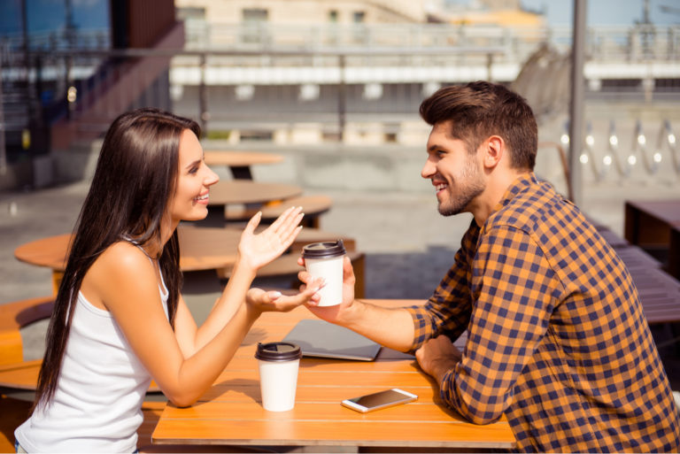 un homme et une femme sont assis à une table à l'extérieur et parlent autour d'un café