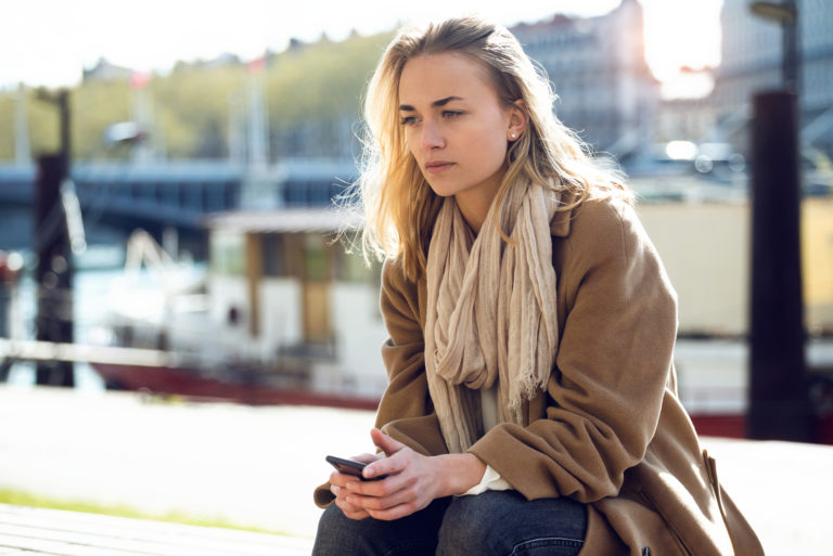 une femme imaginaire aux cheveux blonds est assise et tient un téléphone à la main
