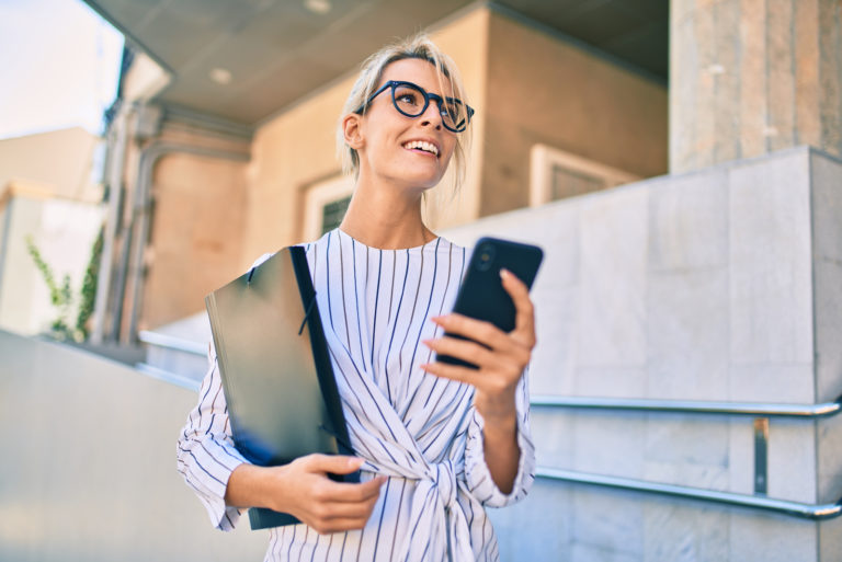 une femme aux cheveux blonde souriante se tient debout et boutons sur le téléphone