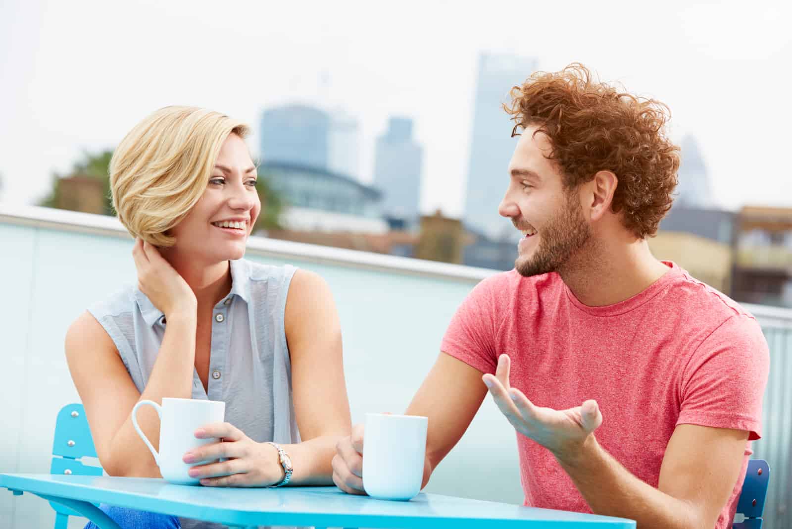 Une femme aux cheveux blonde souriante assise à l'extérieur avec un homme et parlant