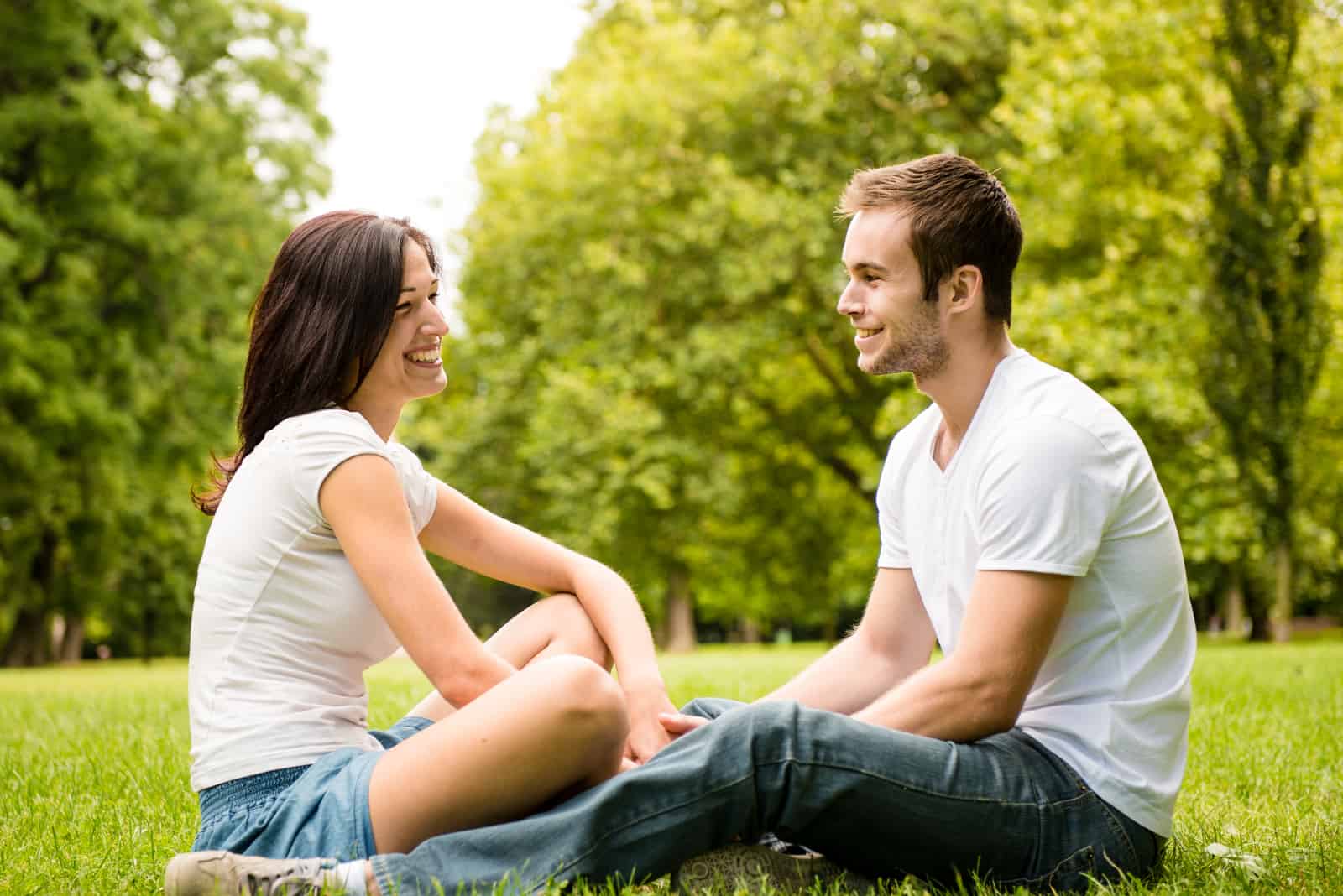 un homme et une femme sont assis sur l'herbe dans le parc et parlent