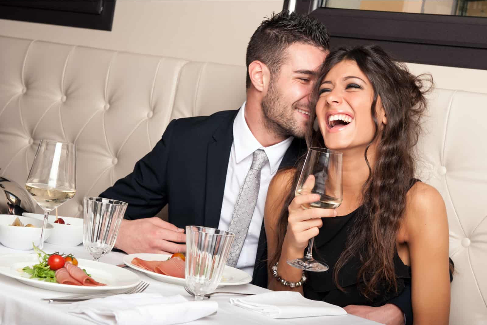 un homme souriant et une femme buvant du vin à table