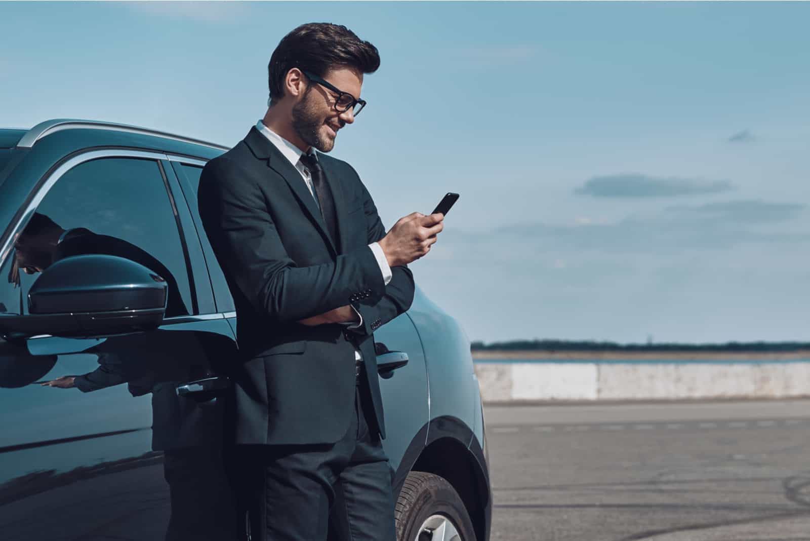 un homme souriant se tient appuyé contre une voiture et un bouton du téléphone
